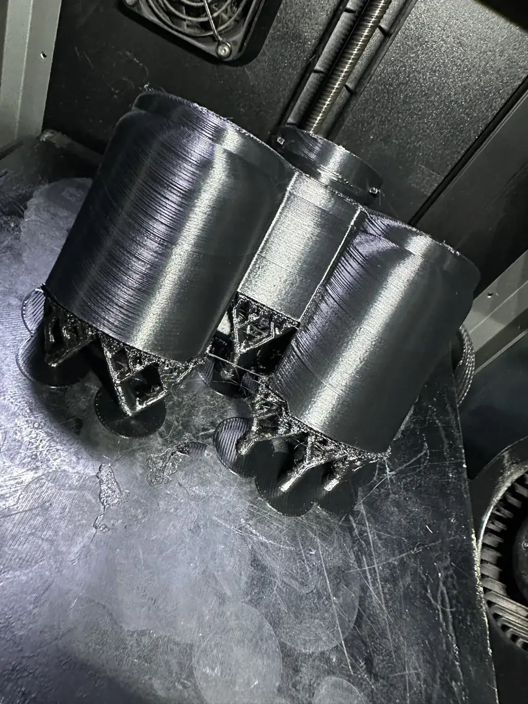 Kapalı kasalı 3D yazıcının tablasında ağaç desteklerle basılmış, çift silindir formlu siyah VW Bora far içi parçası